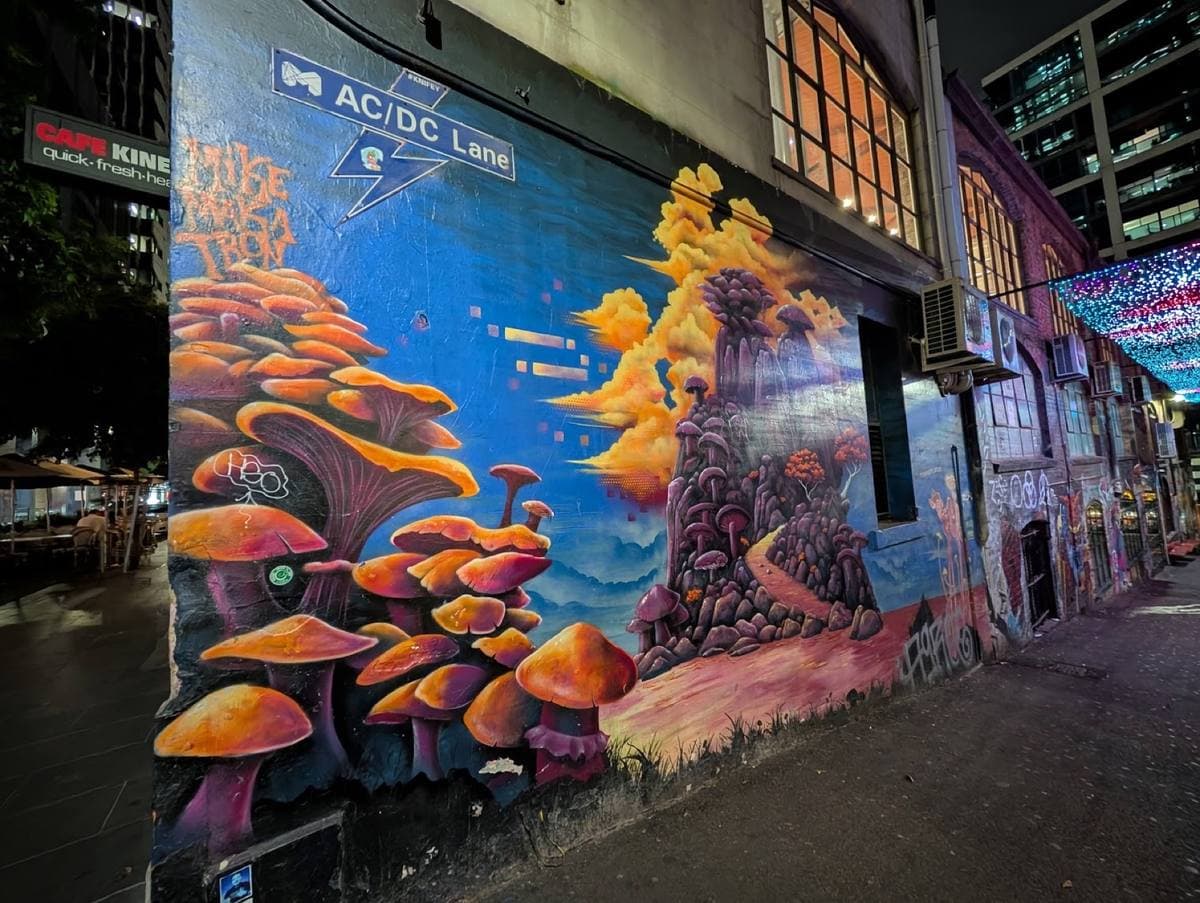 A lane wall painted with orange mushrooms under a blue street sign