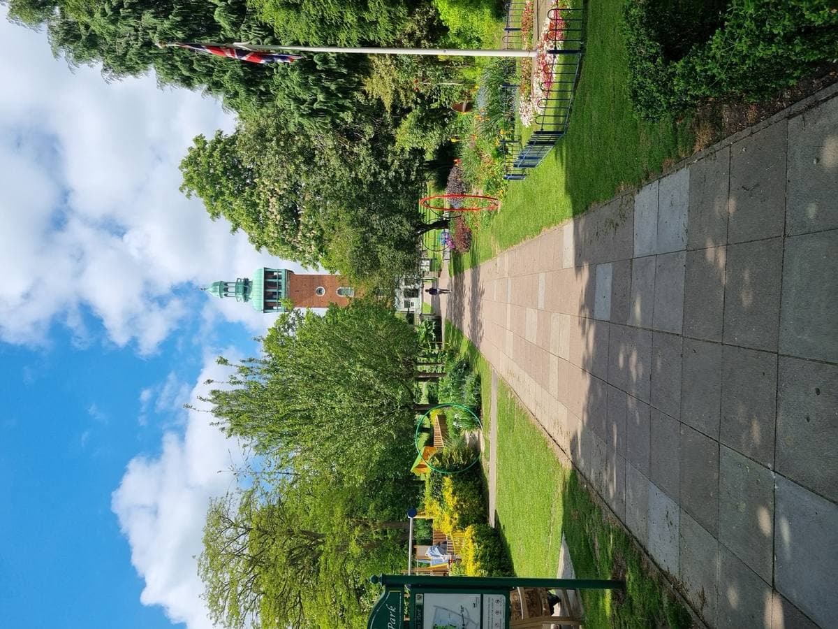 A brick bell tower with a green copper top at the end of a park path