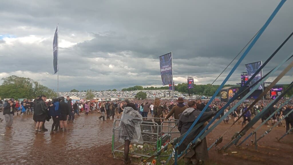 Festival-goers in a muddy field under grey skies and flags