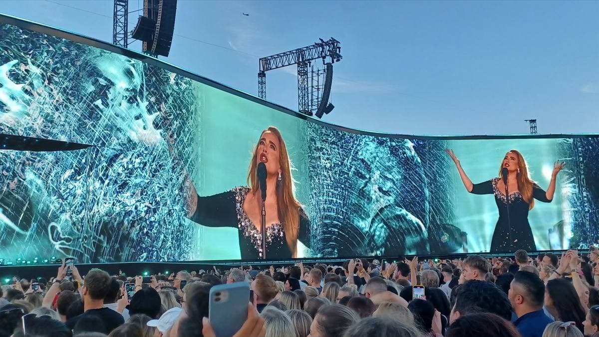 A huge curved screen shows Adele twice over a packed crowd at dusk in Munich