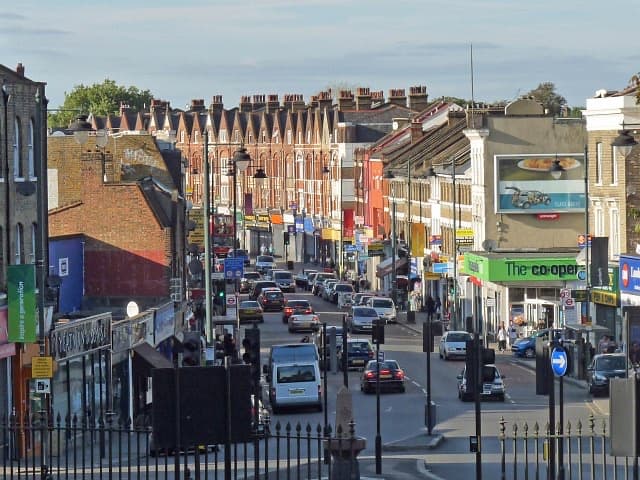 Norwood Road running downhill between rows of shops and terraced houses on a sunny evening