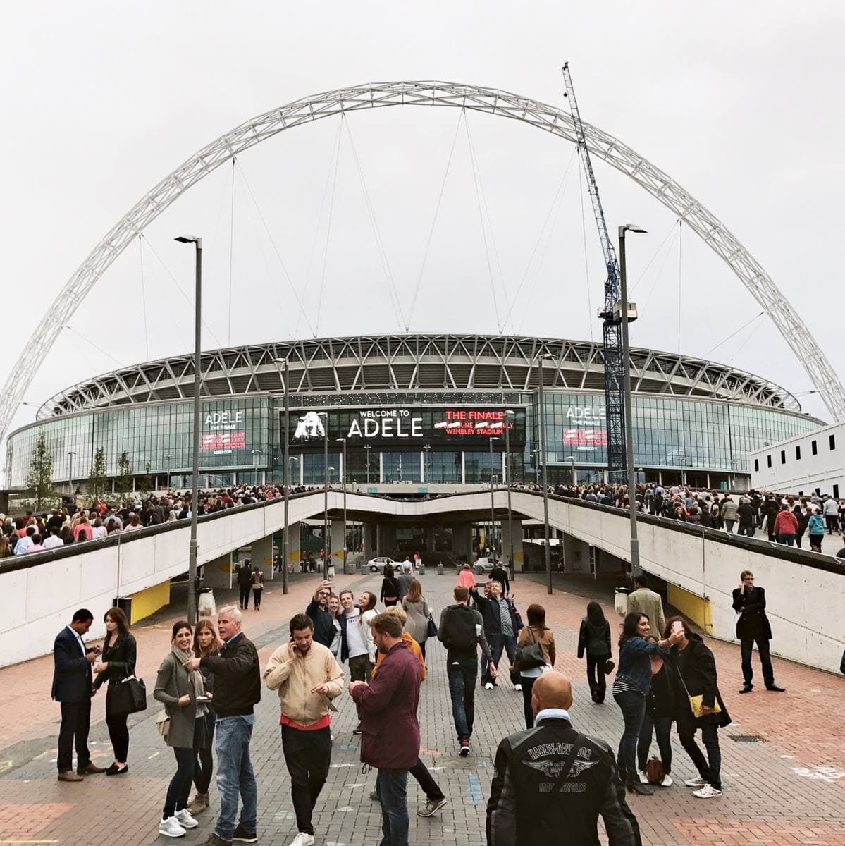 Crowds walk towards Wembley Stadium under its white arch, an ADELE banner across the front