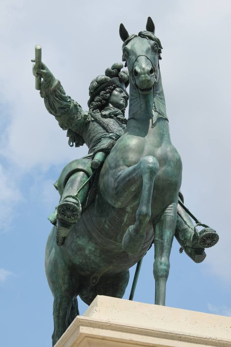 A bronze equestrian statue on a tall plinth under a blue sky in front of the palace