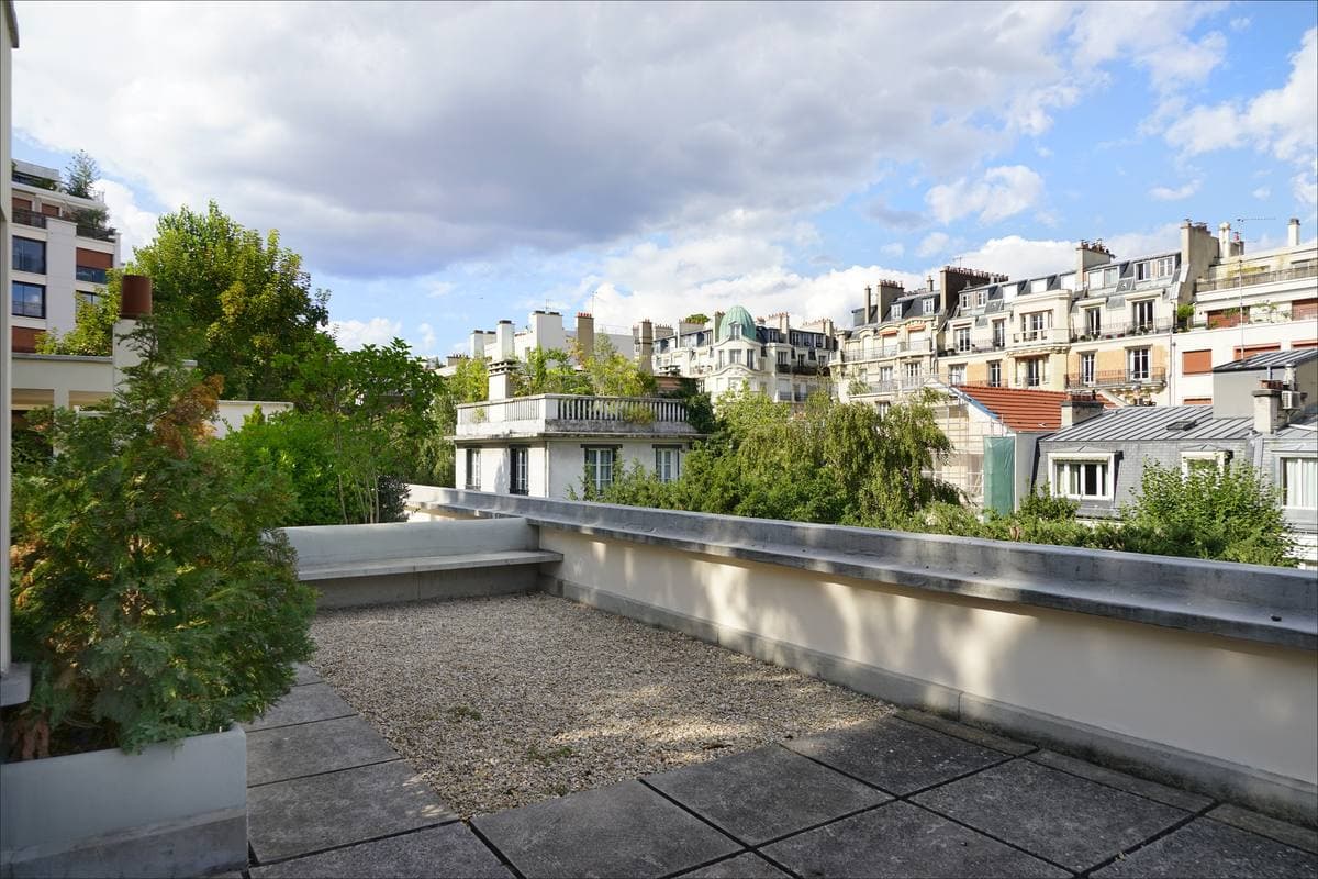 A white modernist roof terrace with a pale rail and green trees beyond