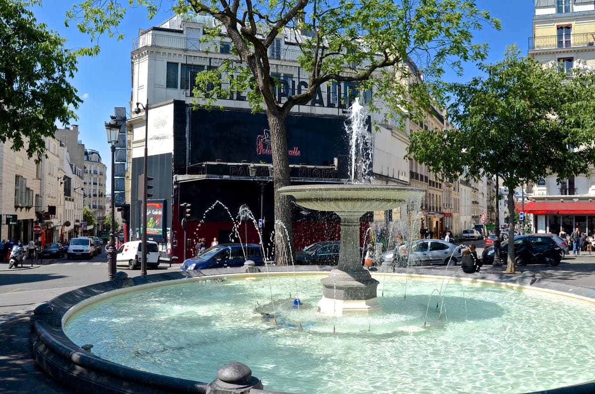 A round fountain in a small Paris square with trees and apartment buildings behind