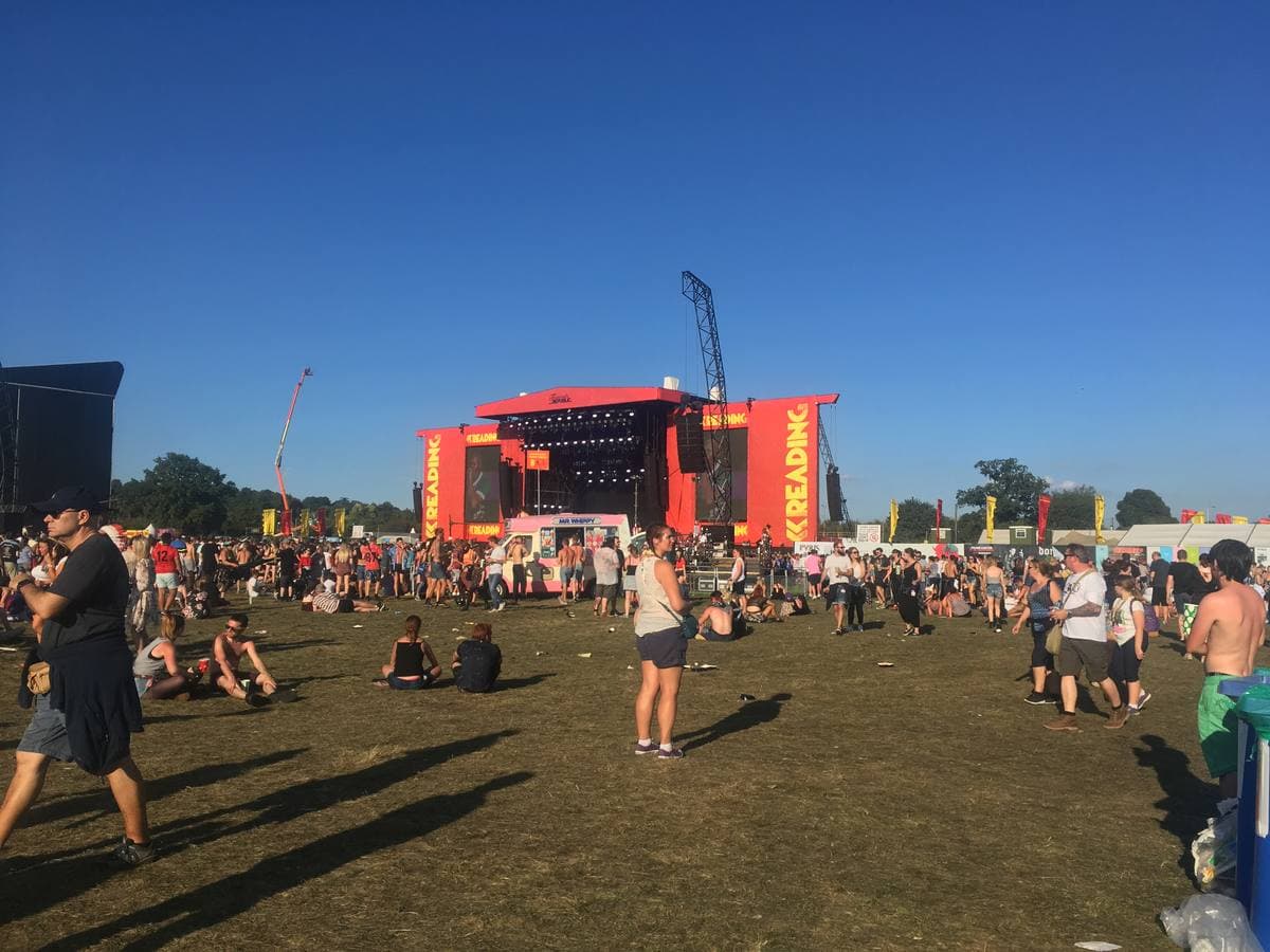 A red and orange main stage across a sunny field, people sitting and standing on the grass