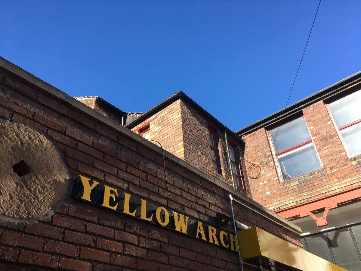Yellow capital letters spelling YELLOW ARCH on a brick wall above a courtyard, blue sky behind