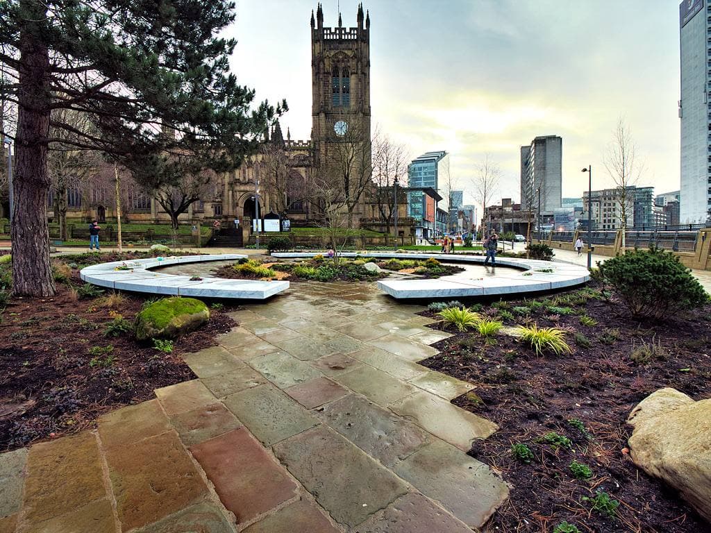 A white stone ring among young trees and planting beside a sandstone cathedral