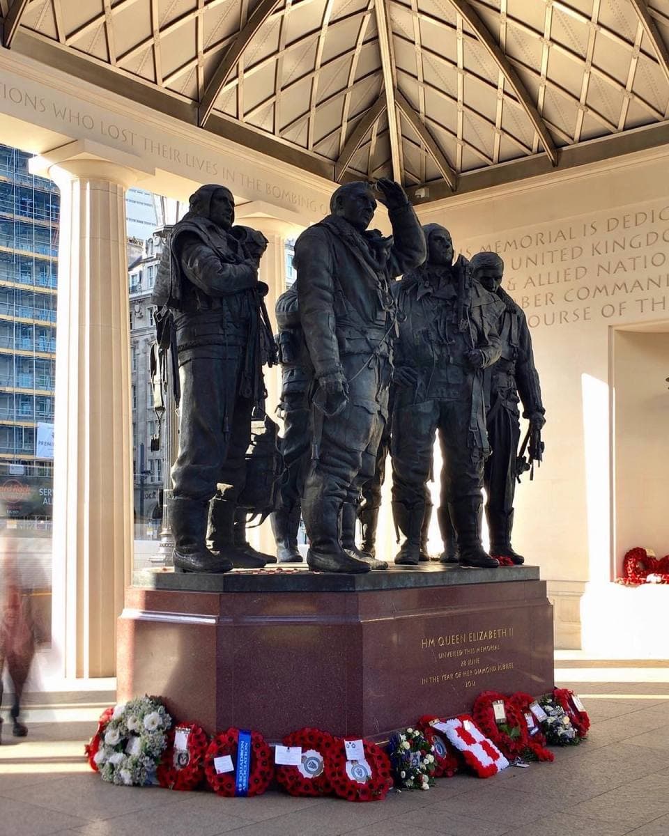 Seven bronze airmen under an open colonnade roof, wreaths at their feet