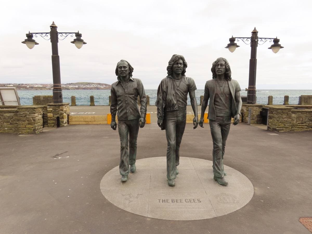 Three bronze figures of the brothers walking side by side on a seafront promenade, the bay behind them