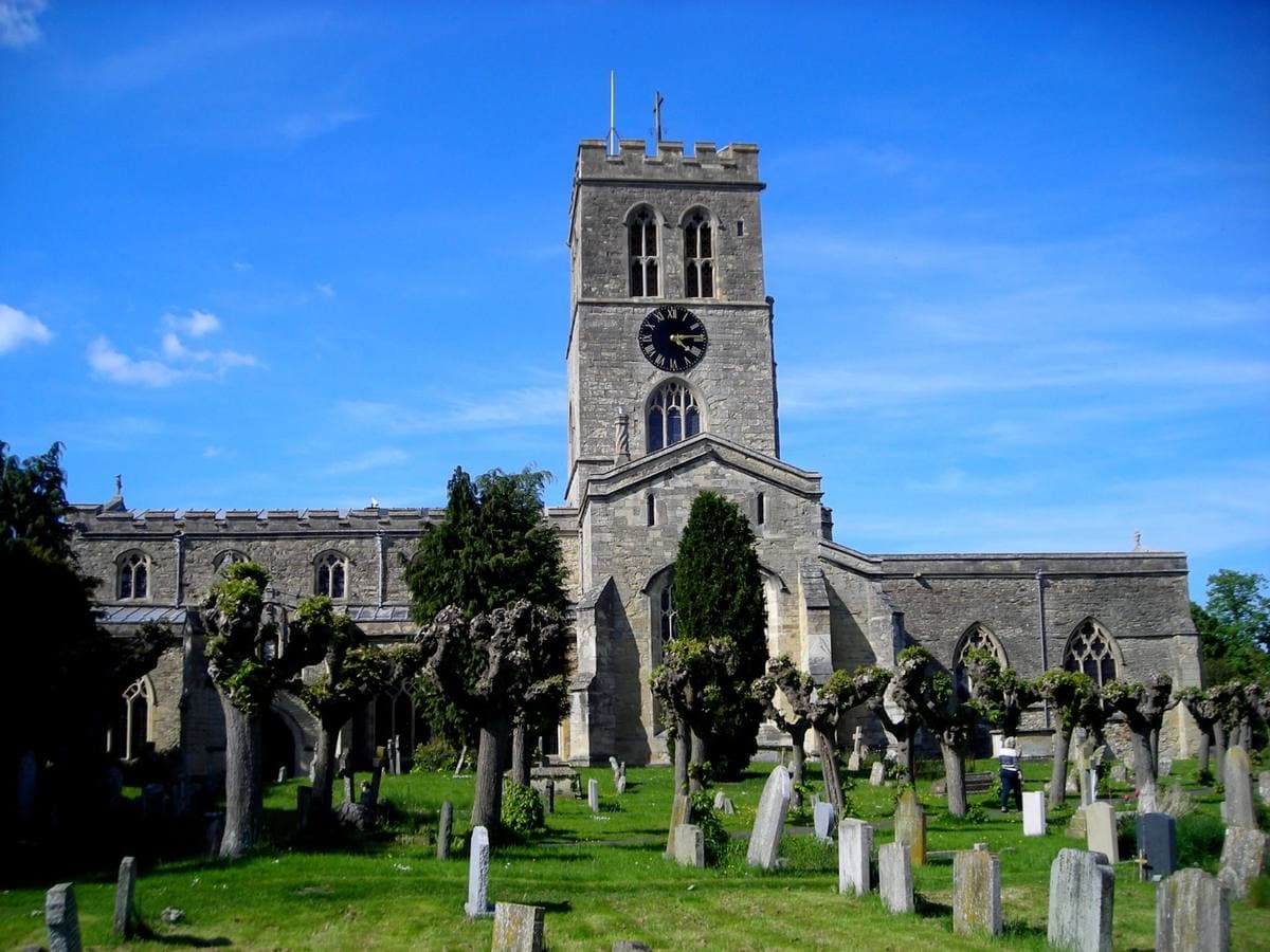 A stone church with a square clock tower above a churchyard of pollarded trees