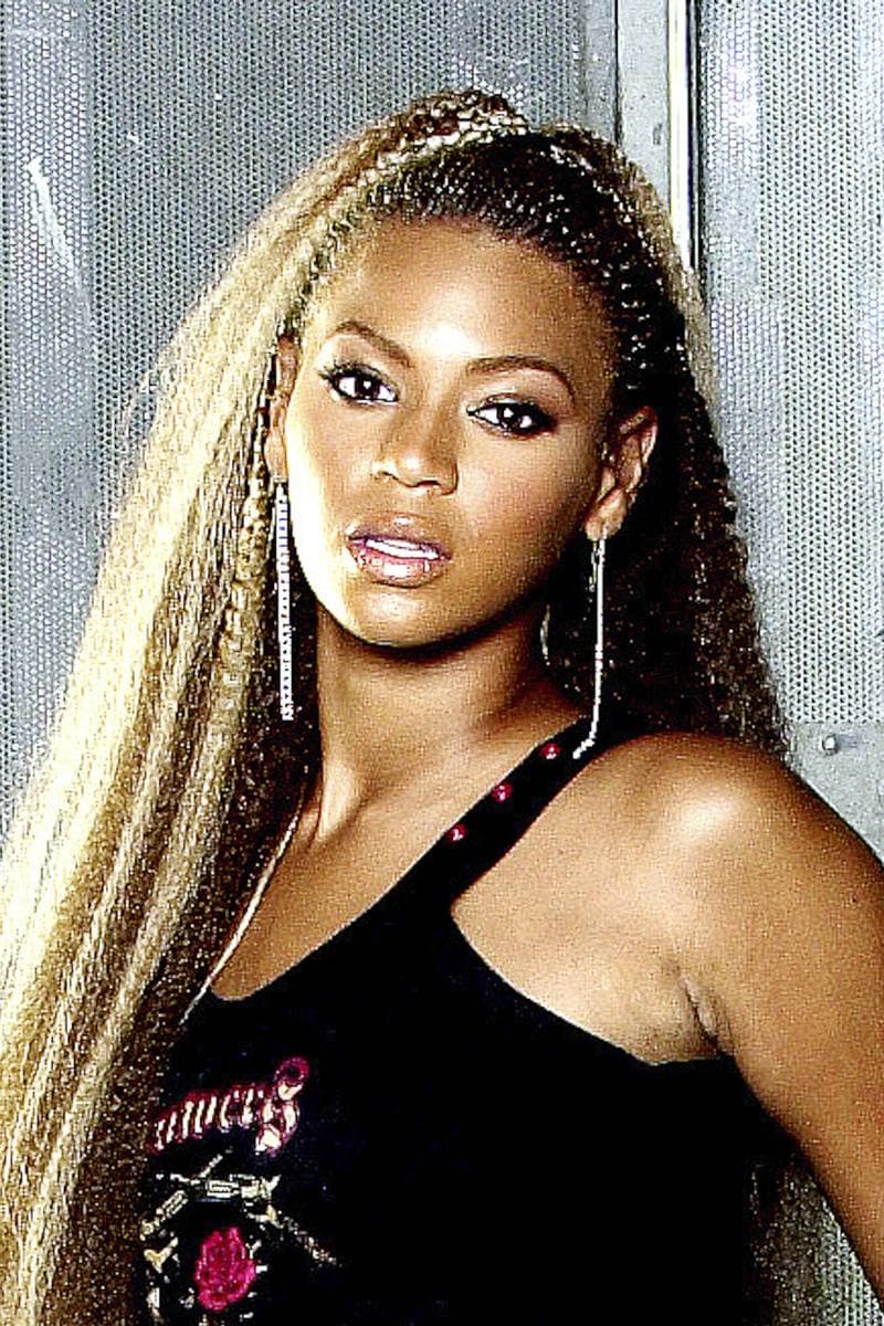 A young woman with long braided hair and gold hoop earrings looks into the camera