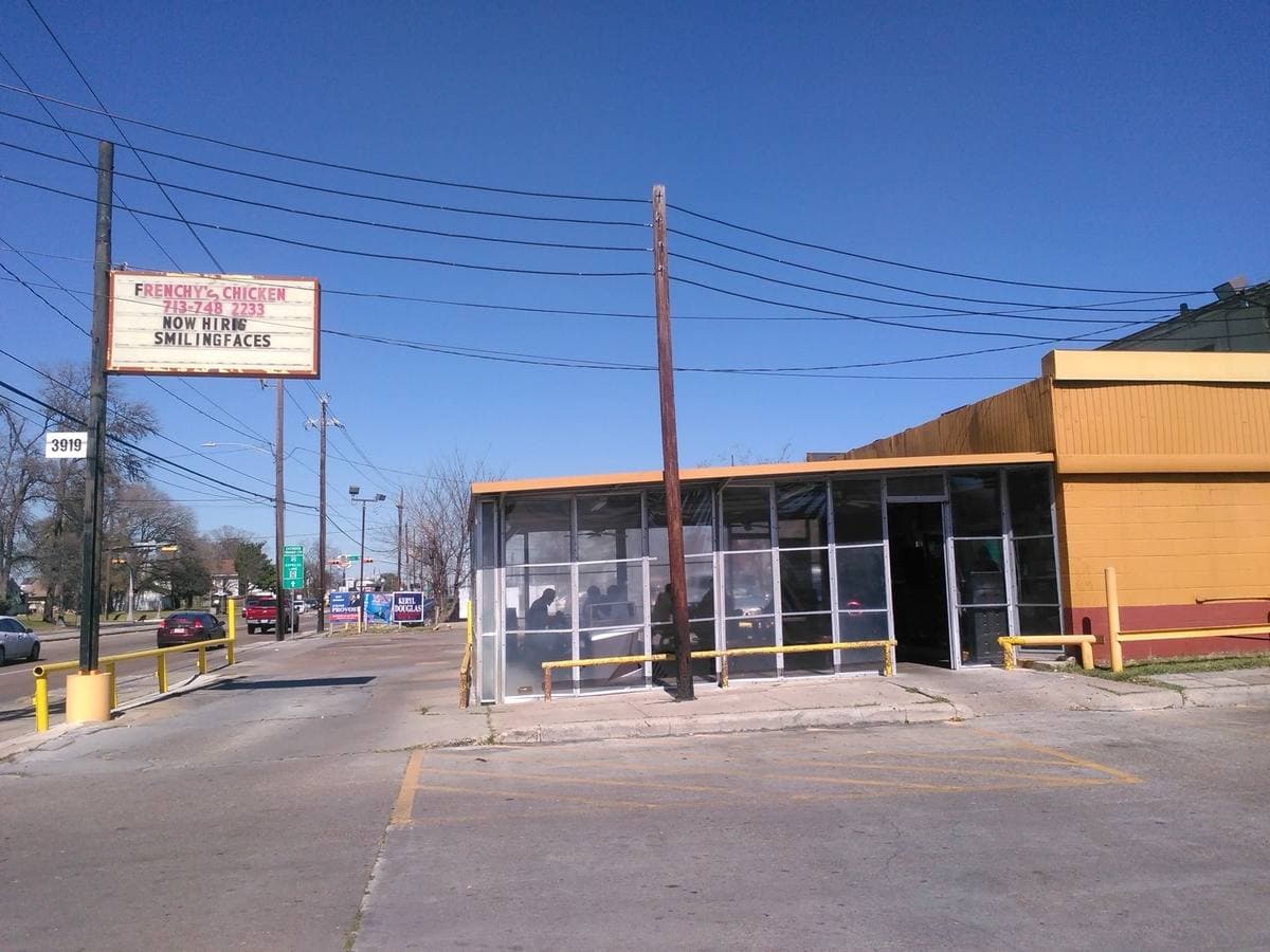 A low single-storey chicken shop with a tall roadside sign under a blue sky