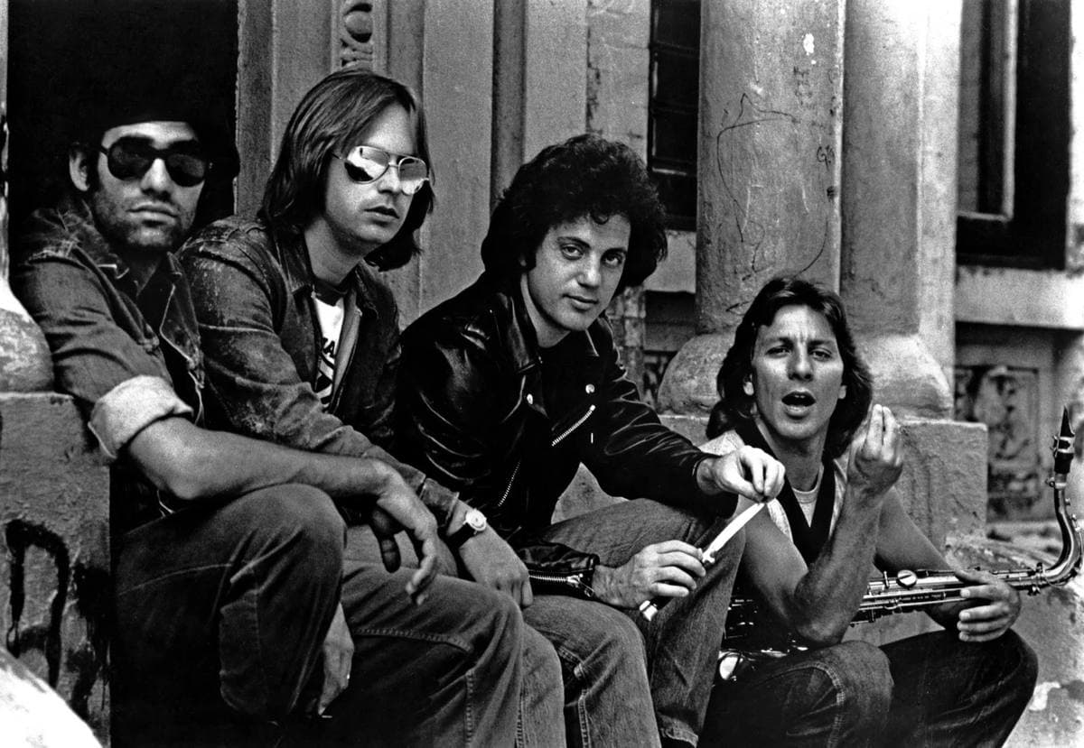 Four men in leather jackets and sunglasses sitting on the steps of a stone building, Billy Joel third from left
