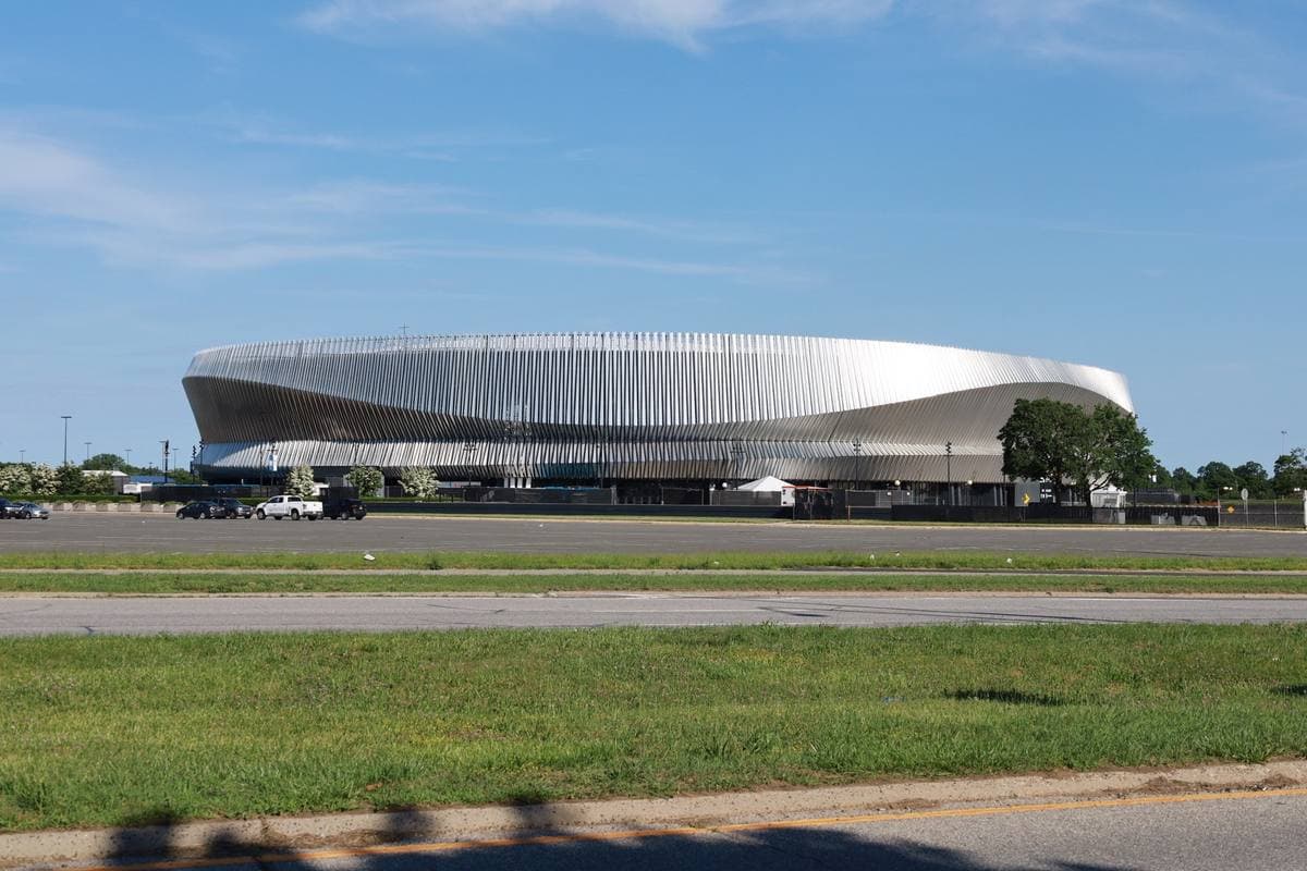 A low round arena with a silver ribbed facade beyond a wide lawn