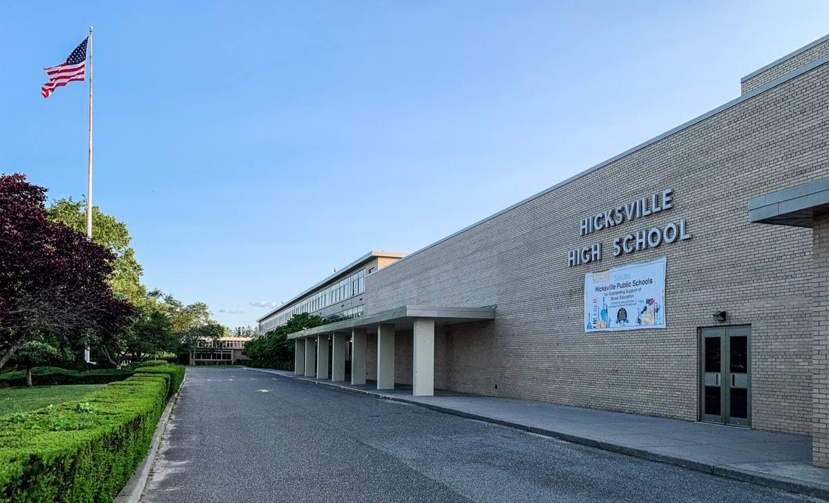 A long low brick-faced school building with its name on the wall and a flag in front