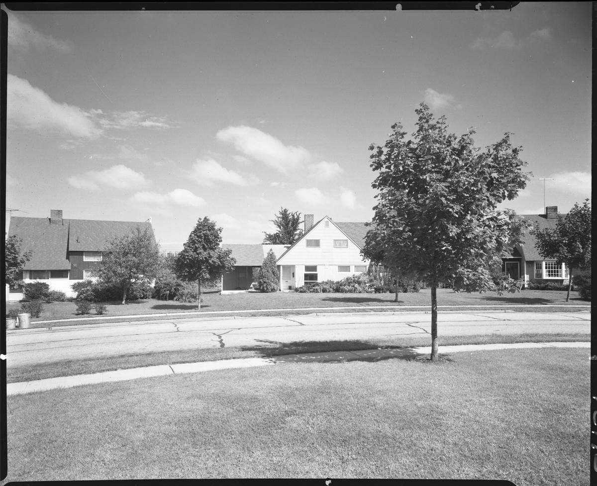 A row of small post-war suburban houses with lawns and a straight path, in black and white