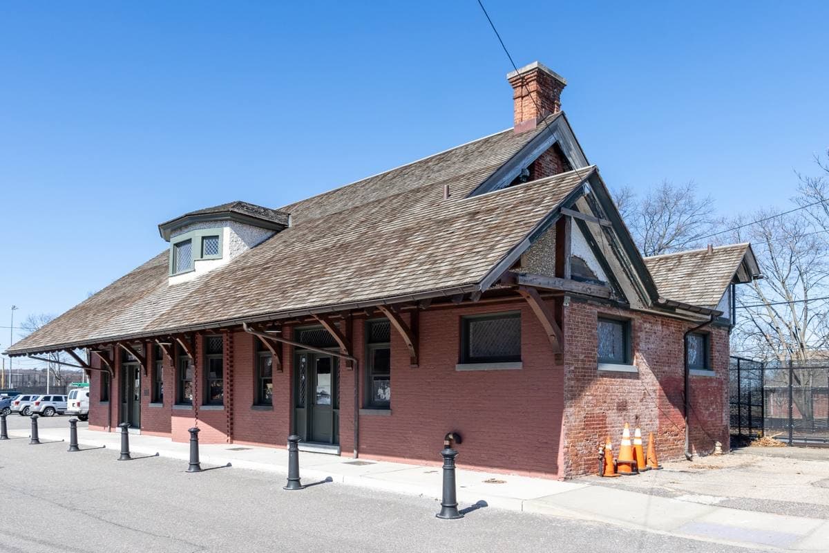 A red-brick railroad station with a steep shingled roof under a blue sky