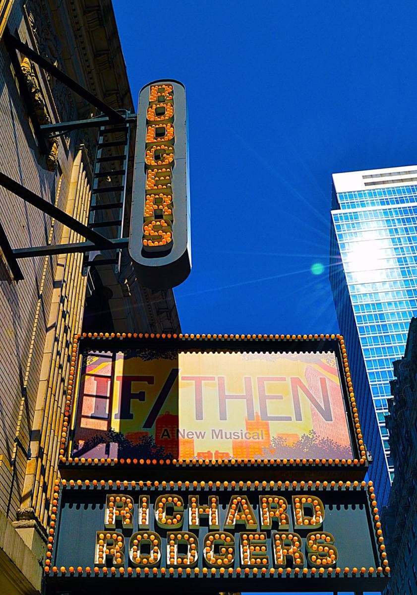 A vertical lit theatre sign reading Rodgers above a marquee at dusk