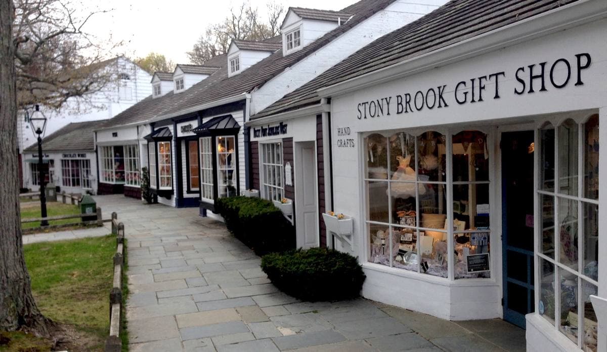White clapboard shopfronts along a paved walk with shrubs