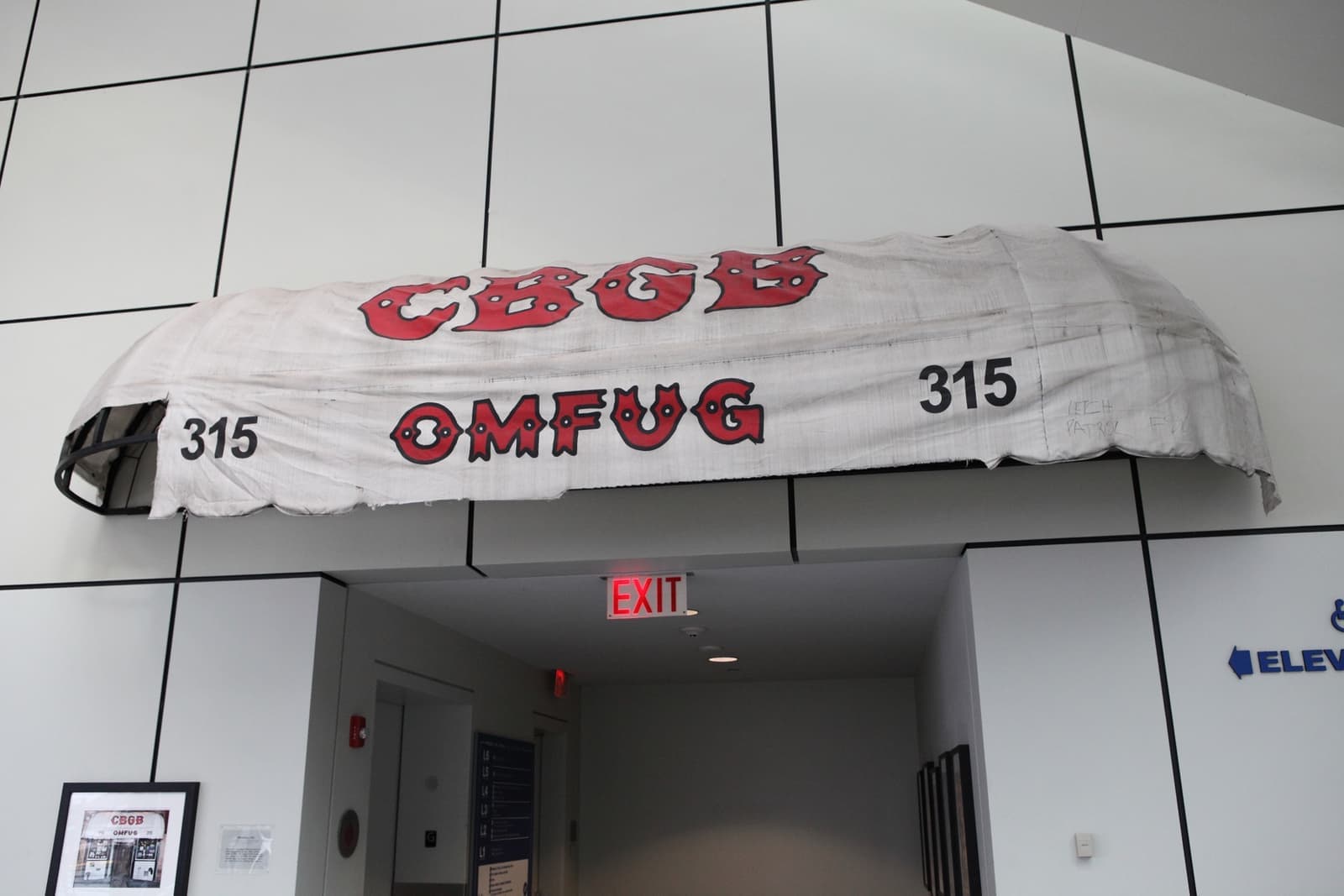 The battered white CBGB OMFUG awning mounted over a doorway in a white gallery