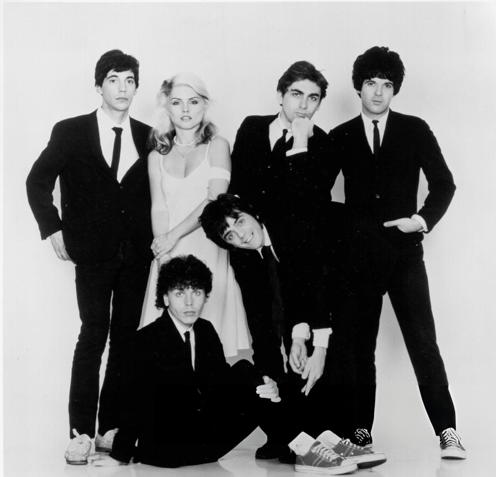 Six band members in black and white, Debbie Harry in a white dress among five men in black suits and thin ties