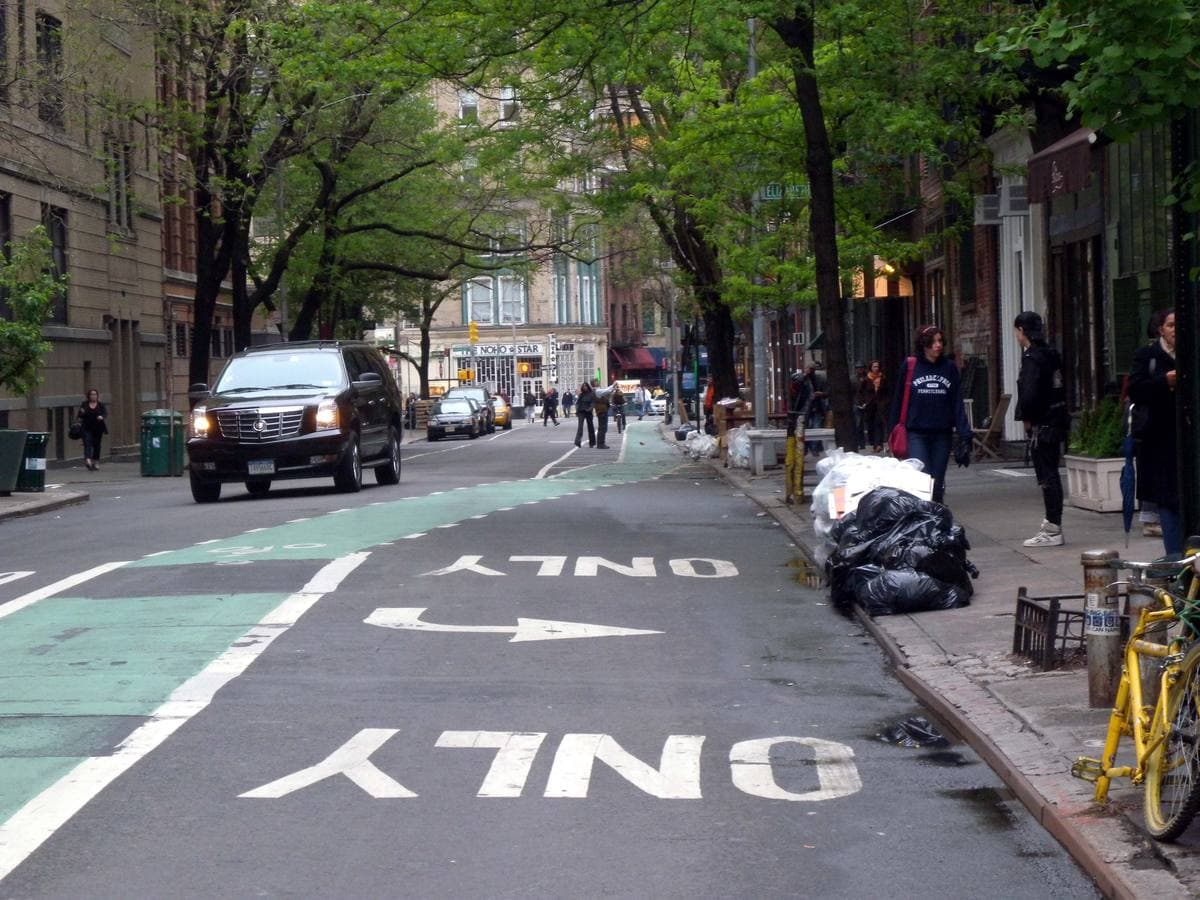 An evening street corner on the Bowery looking west along Bleecker Street, low brick buildings and parked cars
