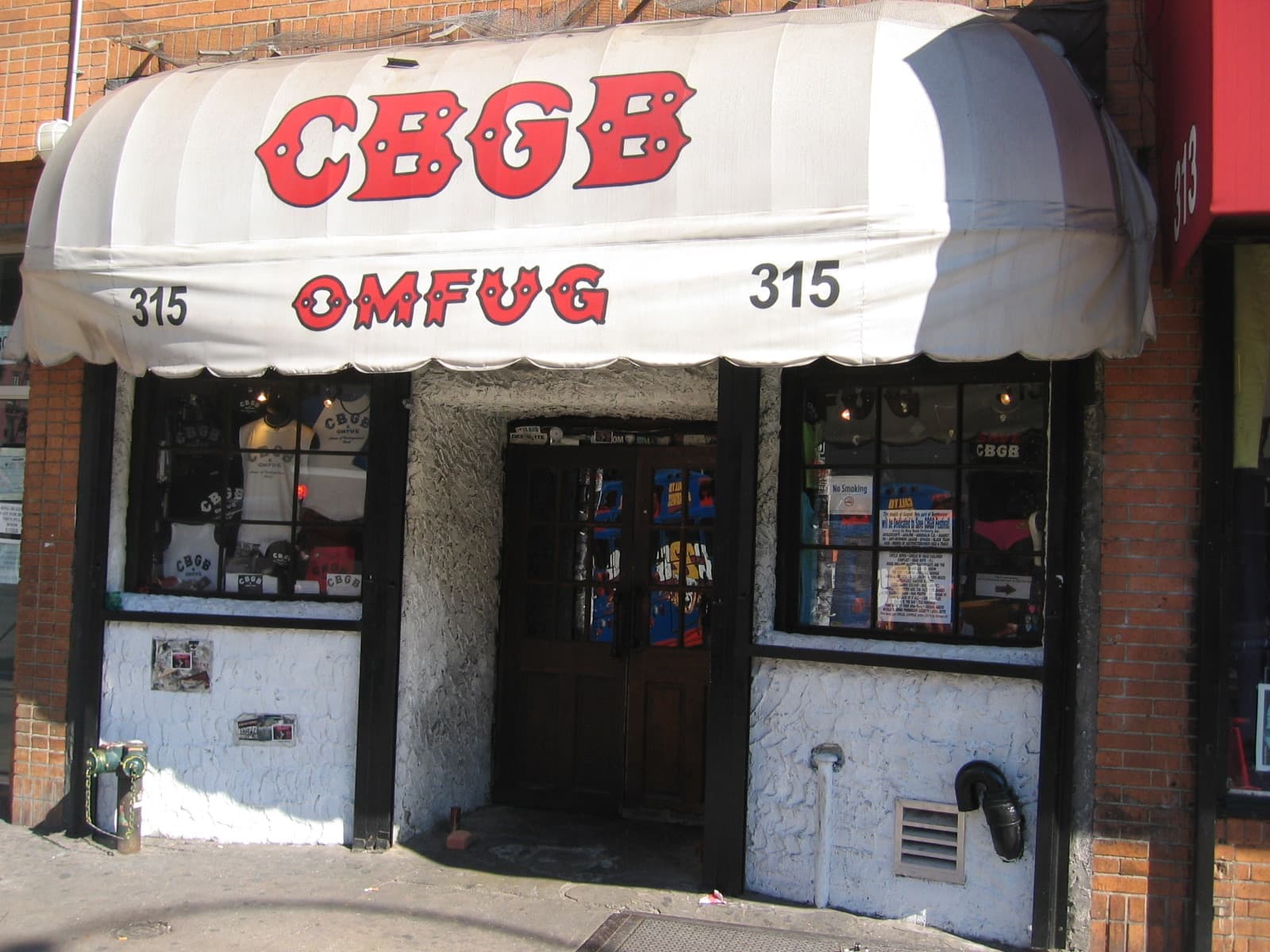 The white CBGB OMFUG awning over a black door plastered in stickers