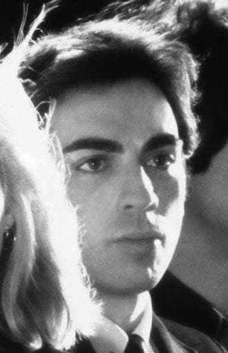 Chris Stein as a young man with dark hair and heavy brows, lit from the side against black
