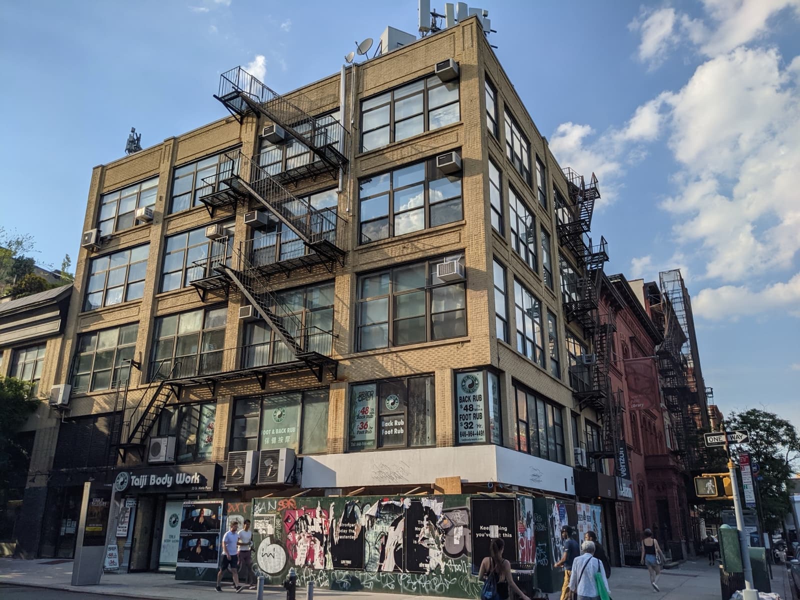 A yellow-brick loft building on a corner of St Marks Place with fire escapes and murals at street level