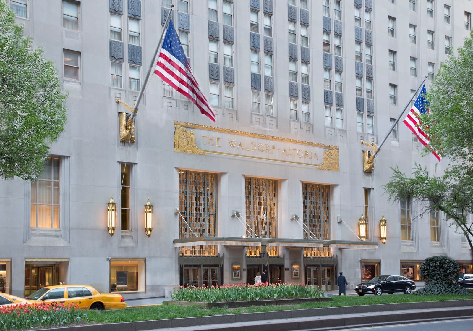 A pale stone Art Deco facade with gilded lettering over the doors and flags either side
