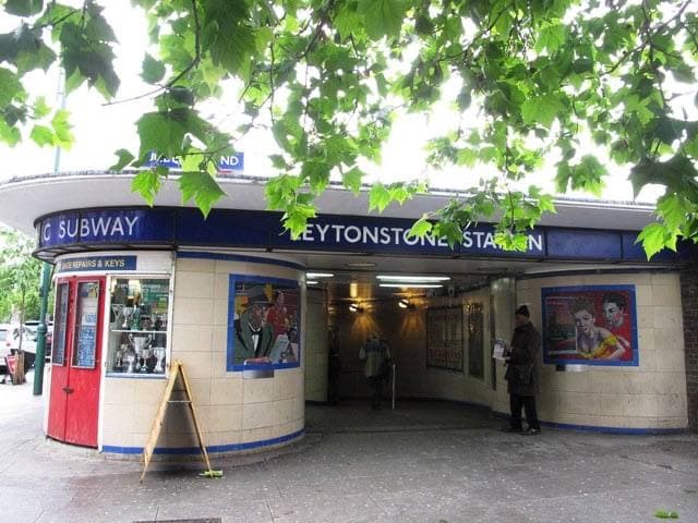 The rounded entrance of Leytonstone Underground station with a blue Subway sign, mosaic panels either side of the door, under plane-tree leaves