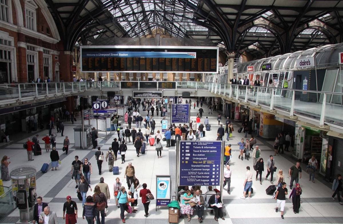 Commuters crossing the busy concourse of Liverpool Street station under an iron and glass roof, the departure board high on the far wall