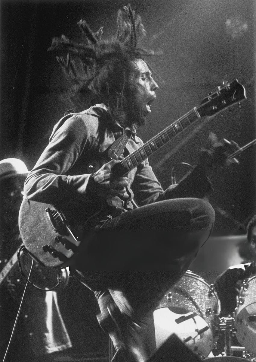 Bob Marley mid-leap on stage with a guitar, dreadlocks flying