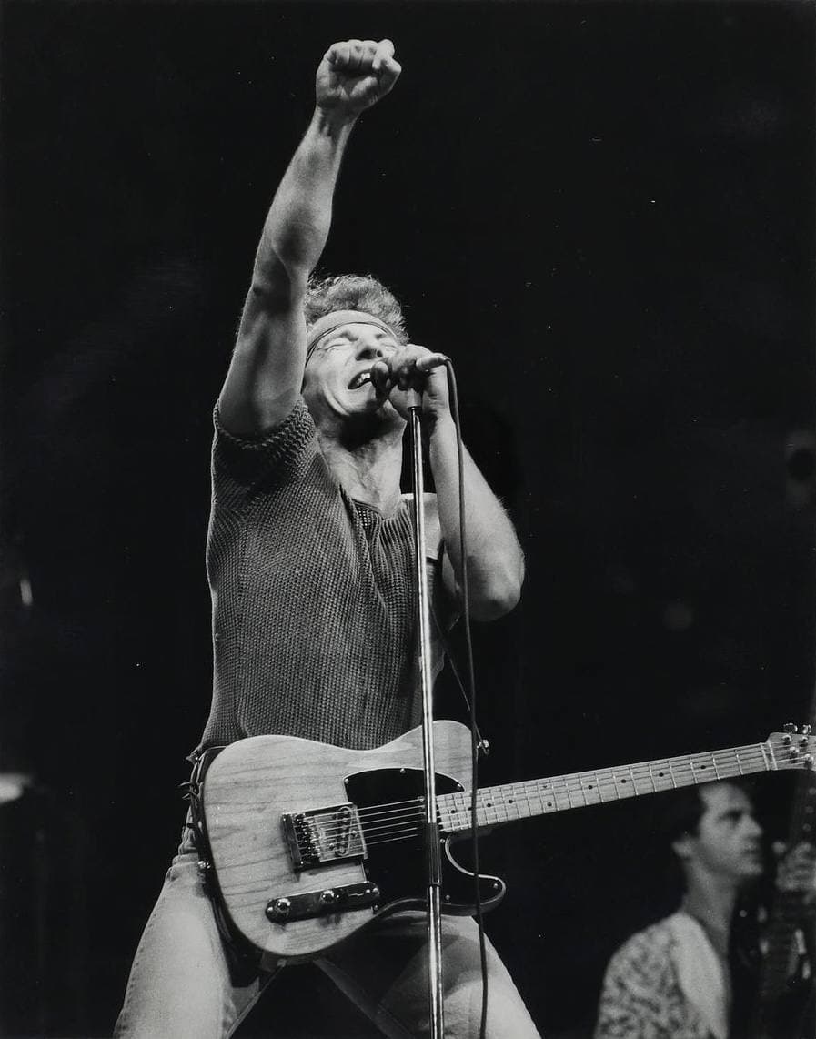 Black and white: Springsteen at the microphone, fist raised high, a Telecaster slung low, in a sleeveless shirt