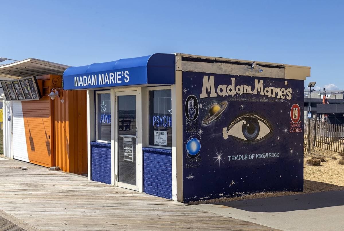 A small blue and white booth on a boardwalk, painted with a large eye and the words Madam Marie’s and Temple of Knowledge