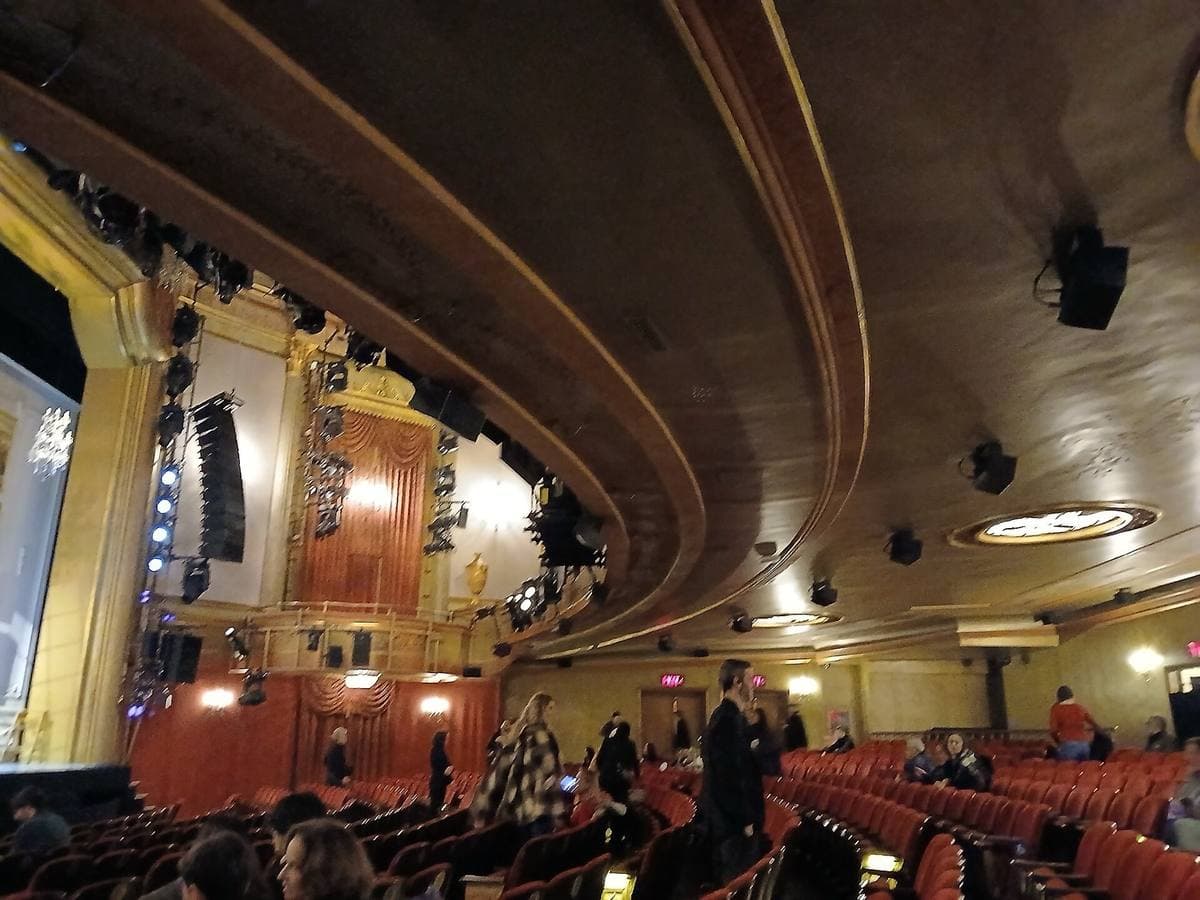 A theatre auditorium with red seats, a deep curving balcony and gilded boxes, the house lights up