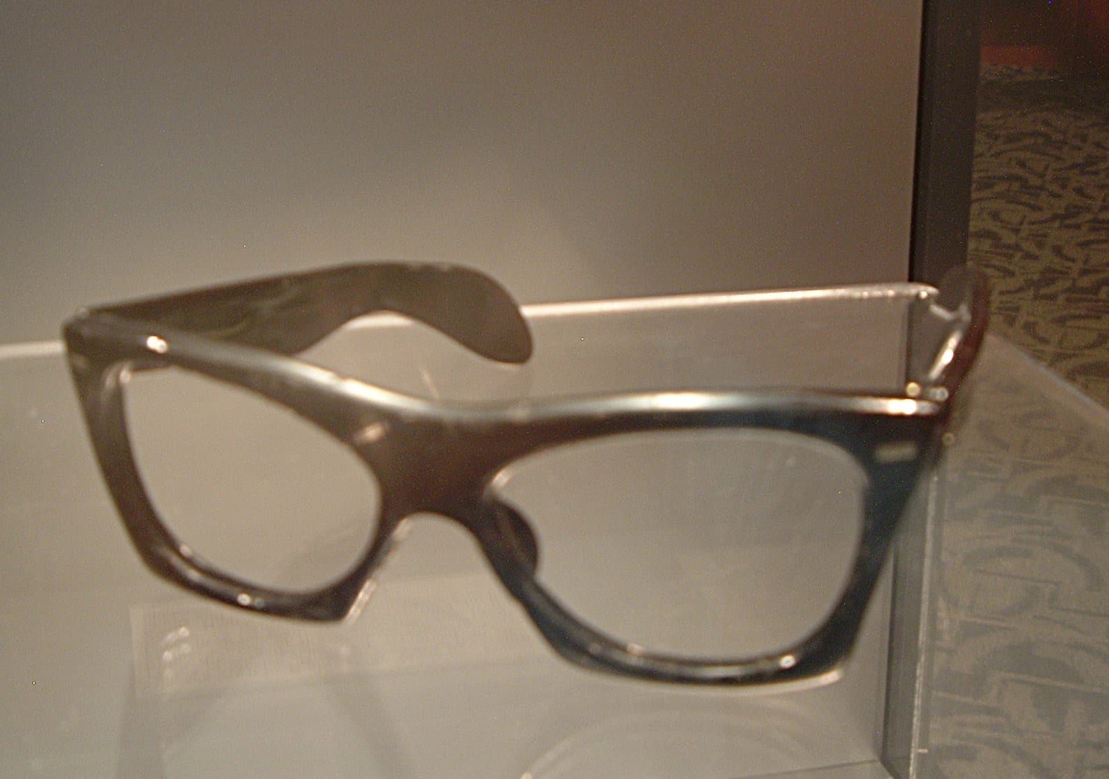 A pair of black horn-rimmed glasses in a museum case