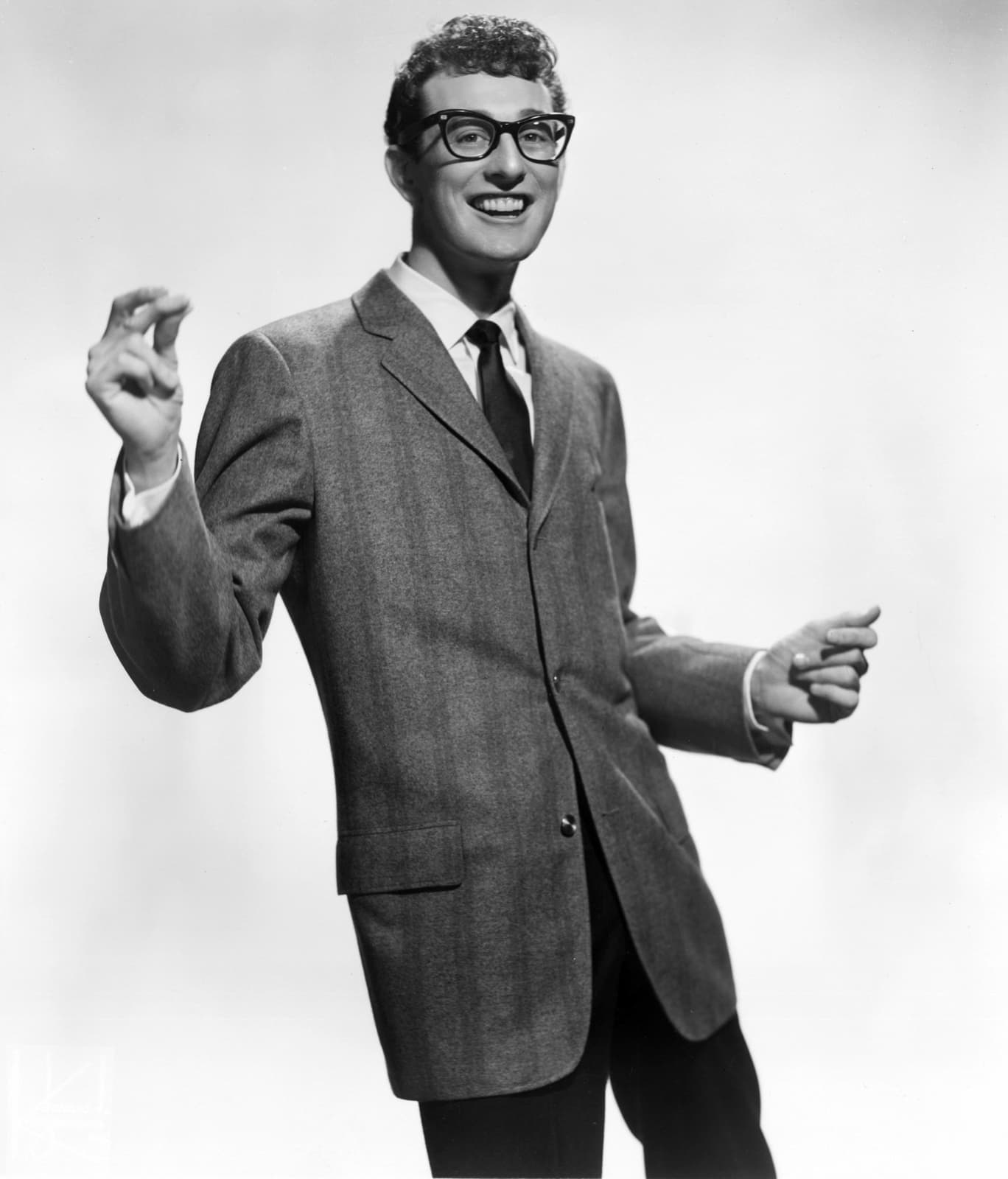 Buddy Holly in heavy dark-framed glasses, smiling, in a jacket and tie