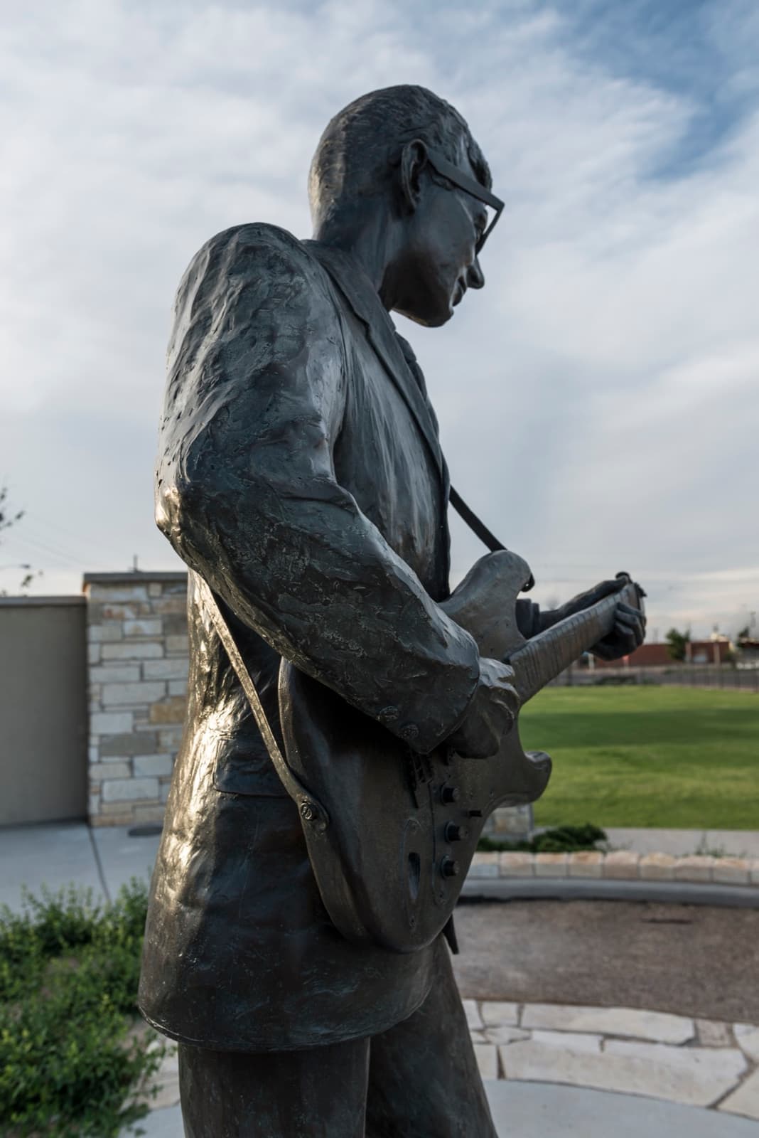 A bronze statue of Buddy Holly playing guitar, seen from below at dusk