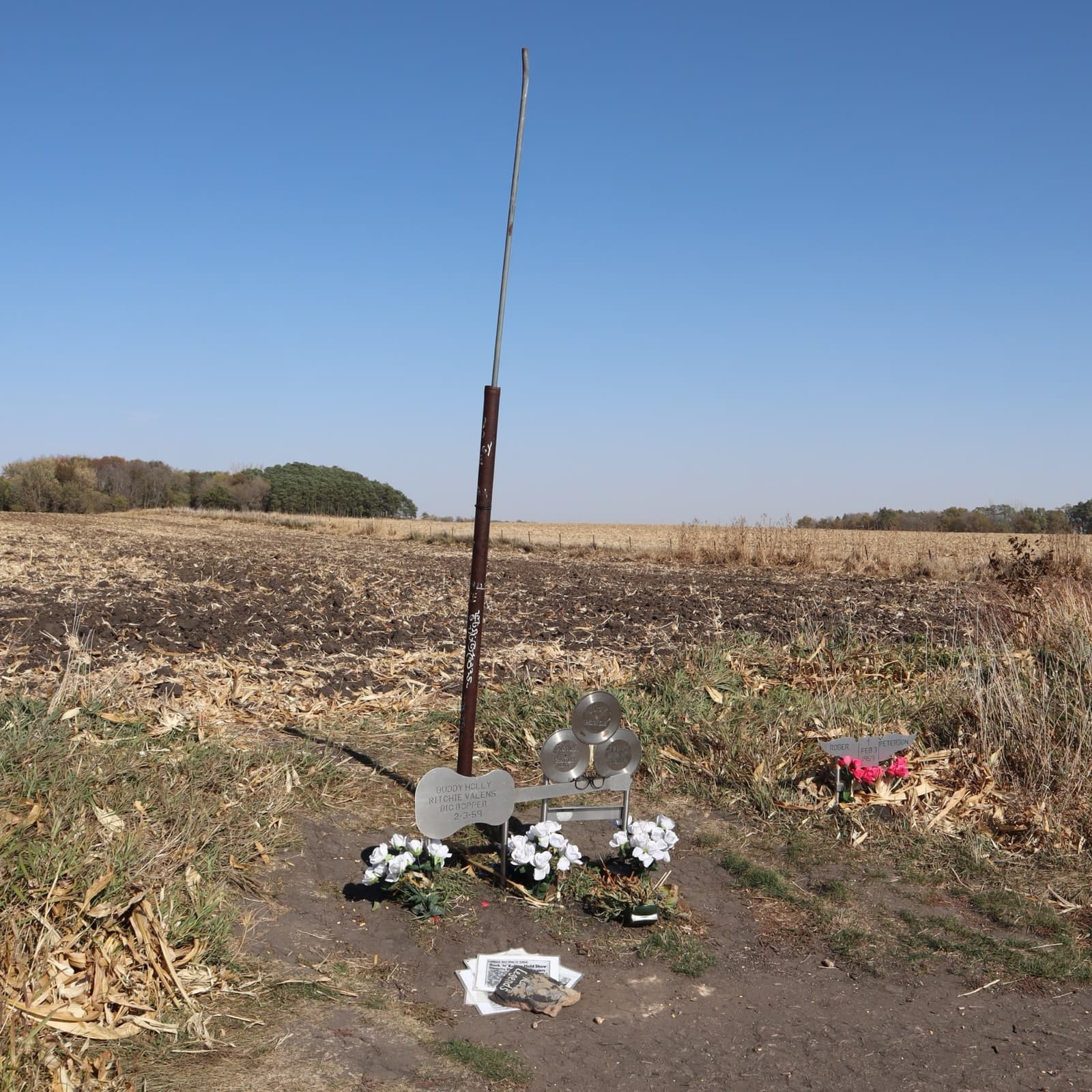 A steel guitar and three steel records at the fence line of a field, with flowers