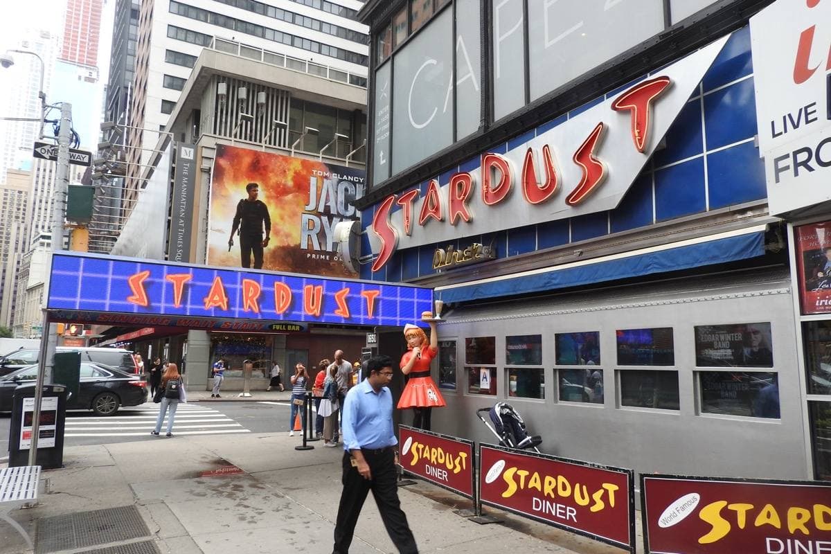 The corner of a tall office building on Broadway with a diner front and awning at street level