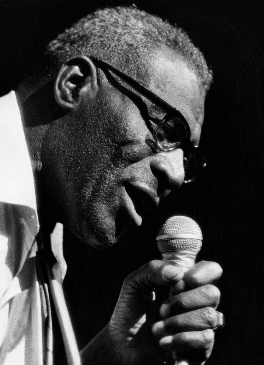 Howlin’ Wolf singing into a microphone, seated