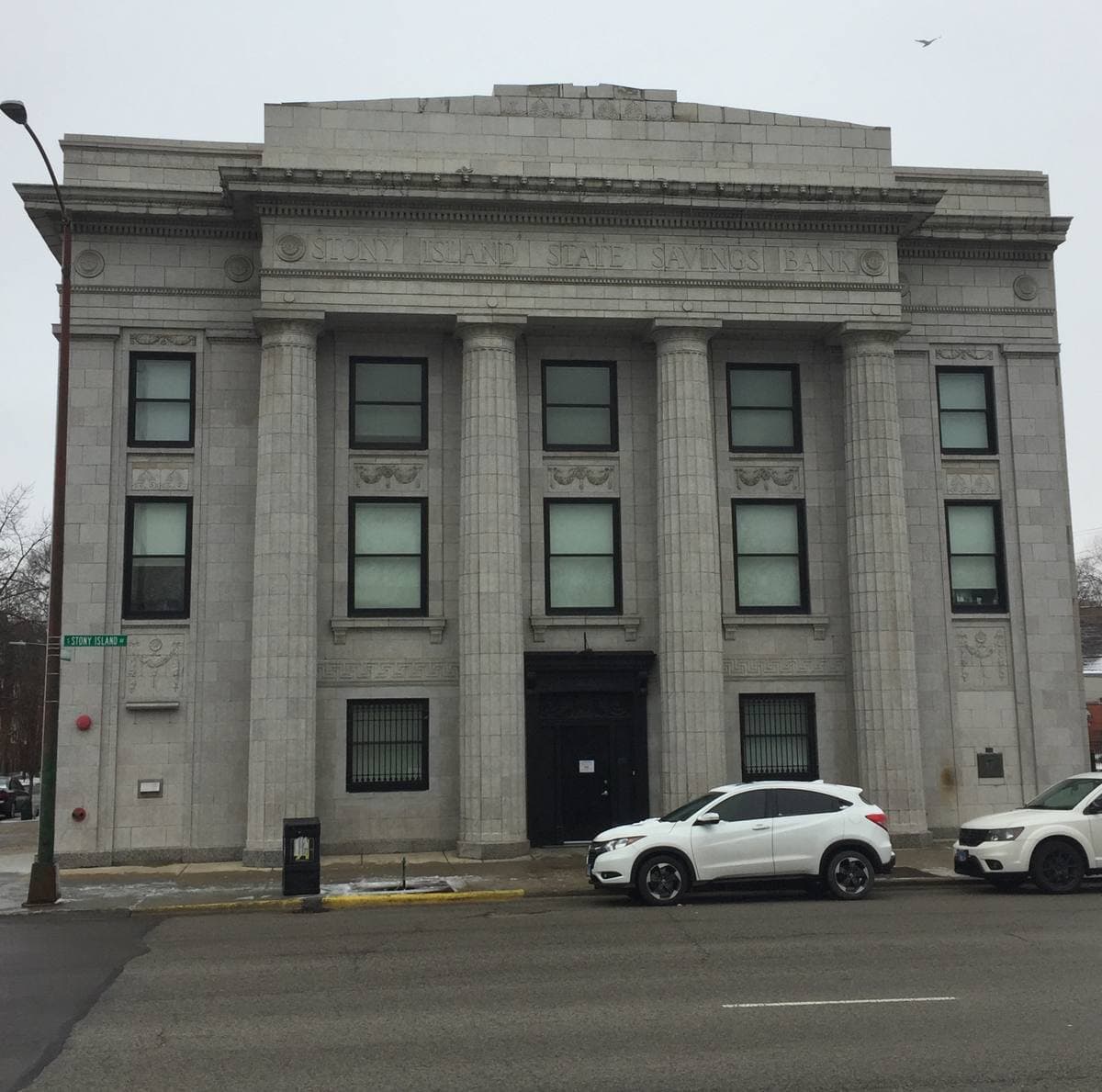 A grey stone classical bank front with tall columns and a parked white car