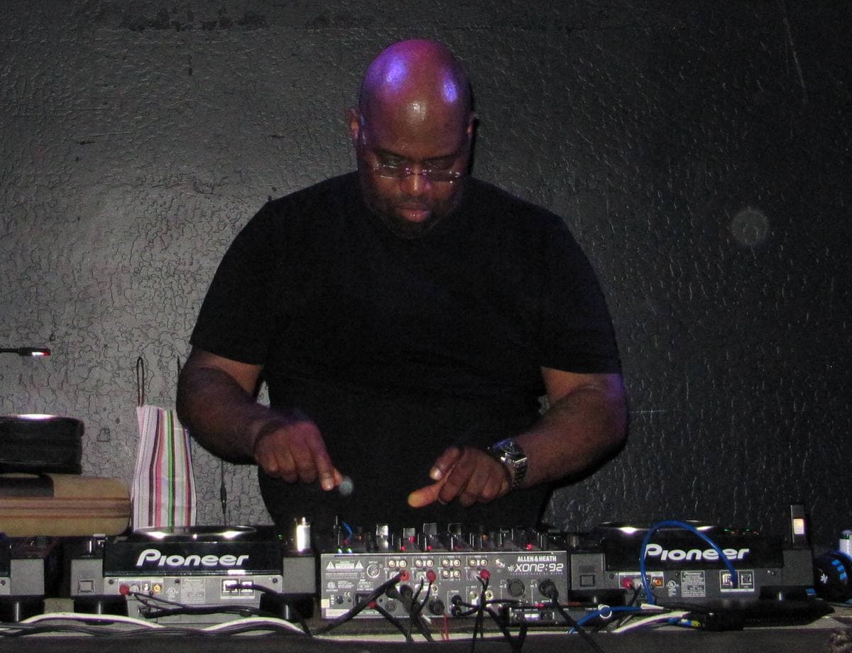 Frankie Knuckles in glasses bent over two Pioneer decks, both hands on the controls