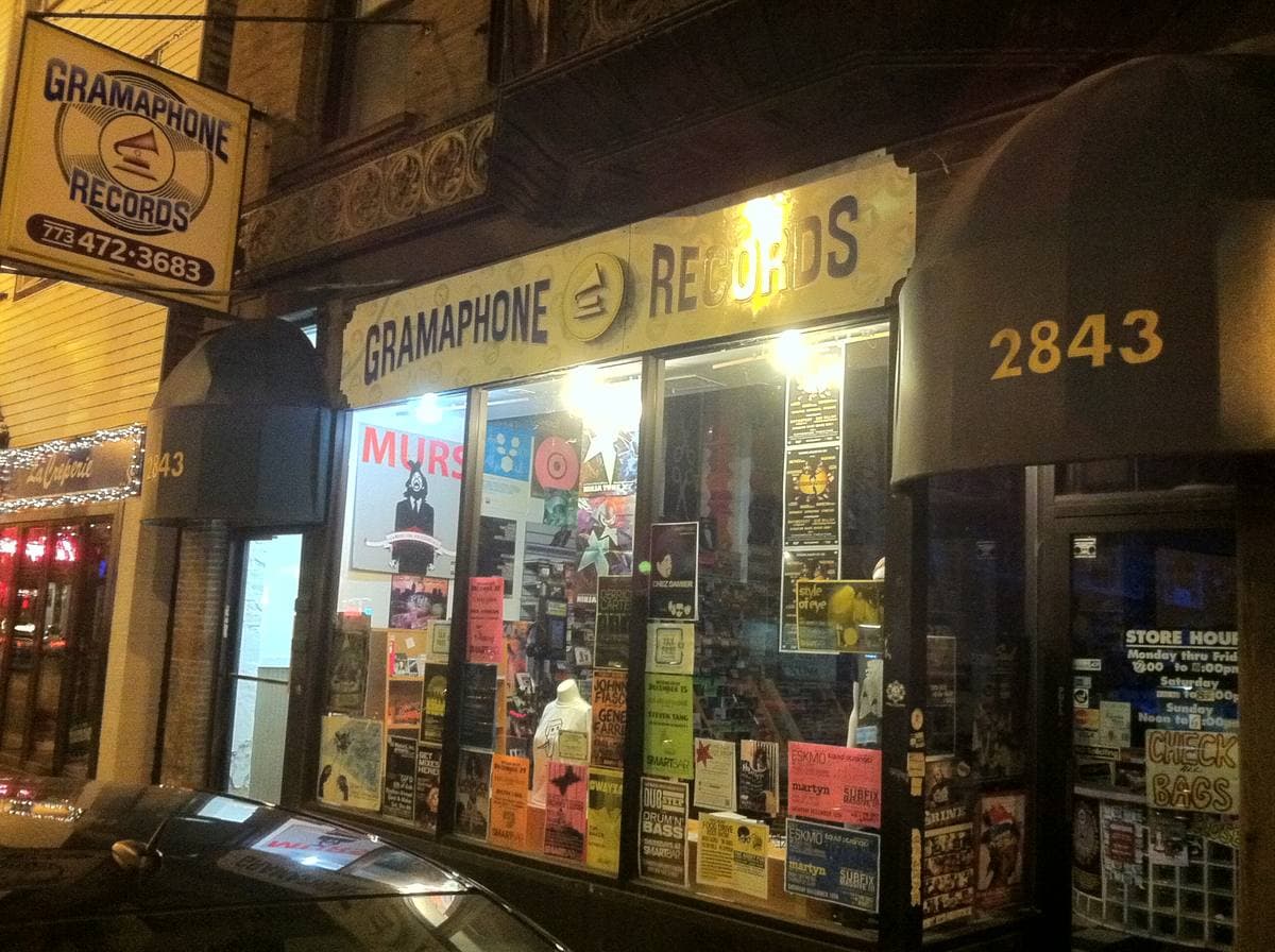 A record shop front at night with a lit Gramaphone Records sign, posters in the windows and the number 2843 on the awning