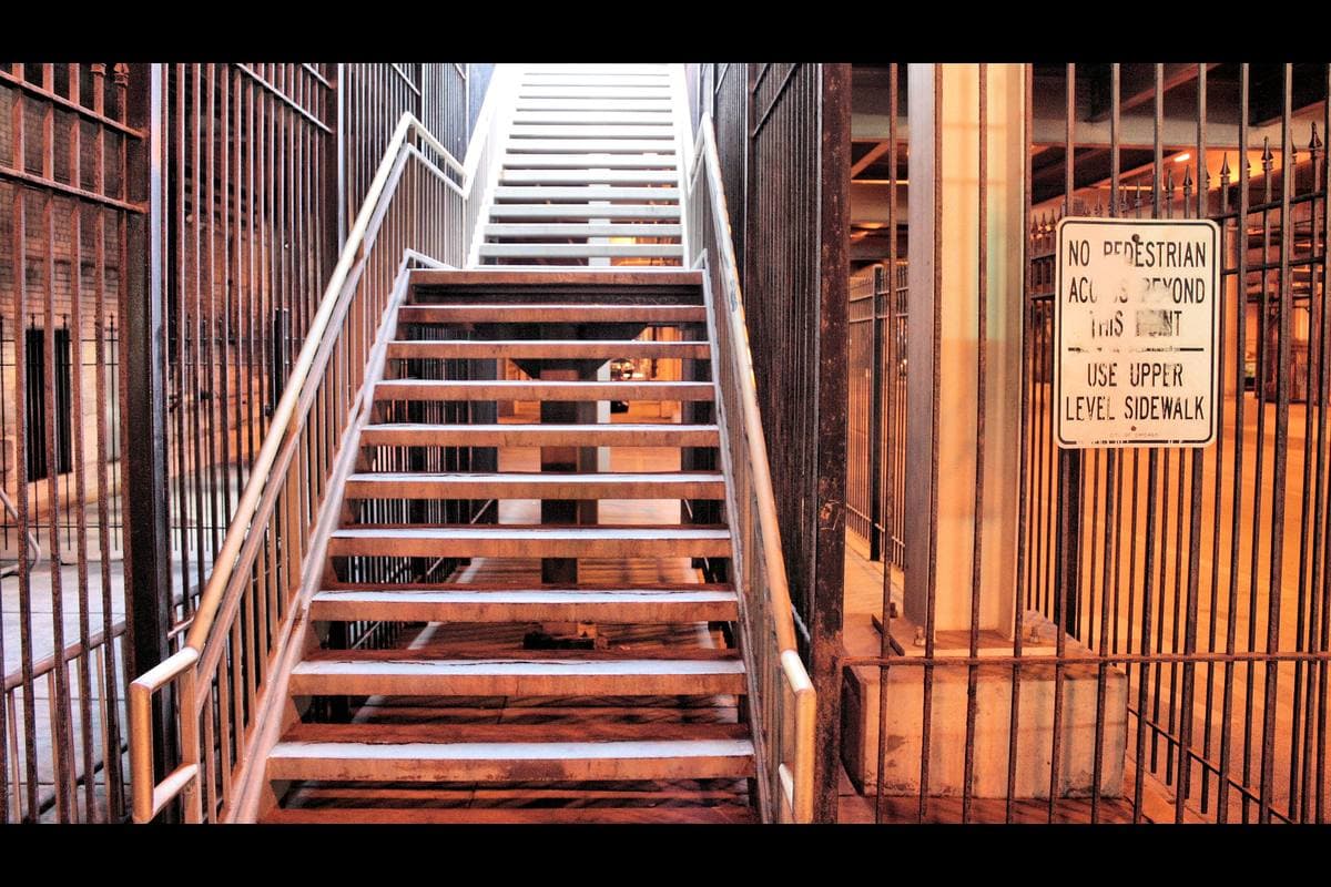 A steel stairway lit orange, rising between barred railings, a sign about pedestrian access at the side