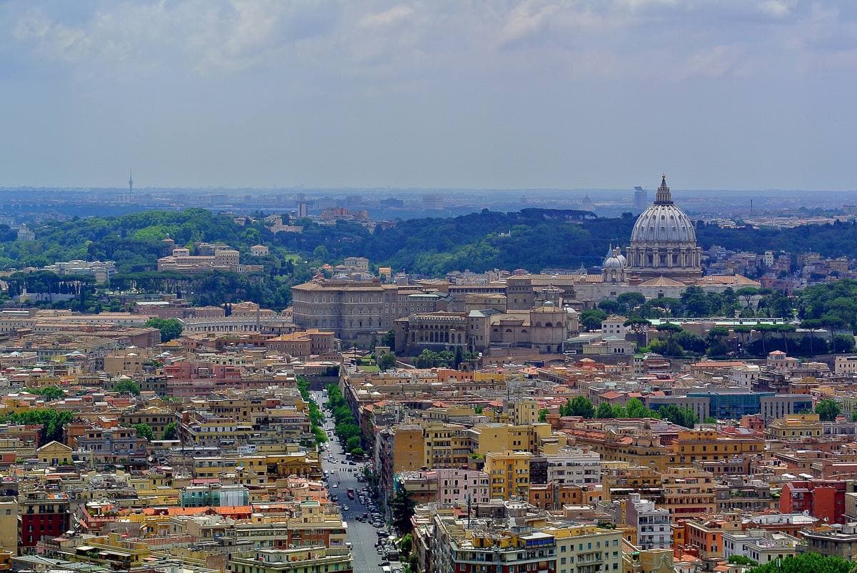 A panorama of Rome’s roofs and green hills from above, with the dome of St Peter’s