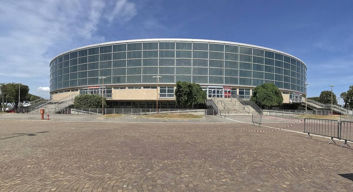A round arena with a glass drum and a shallow ribbed dome above trees