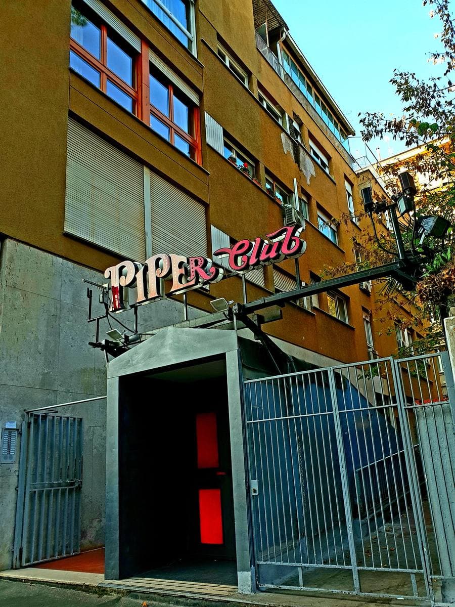 A dark doorway with a red sign reading Piper Club set into an ochre building